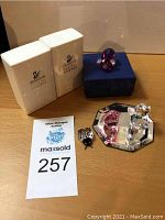 Full lot with white Swarovski boxes and blue box, four crystal figurines including pink pig, pink rabbit, rocking angel, and ladybug on mirror base.