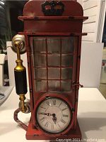 Full view of red telephone booth style clock with gold and black handset on left side and clock face at the bottom.