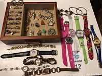 Full lot overview with rings and earrings organized in a felt-lined jewelry drawer insert, bracelets and charms inside drawer compartment, watches laid out on table.