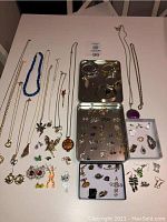 Top view showing assorted jewelry including necklaces, earrings, brooches, and watches in open tins and laid out on white surface