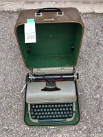 Full view of Remington Quiet-Riter typewriter inside the open green-lined brown carry case on pavement.