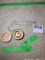 Full view of gold chain, pendant, open round case lid, green tape marked 10K and auction tag