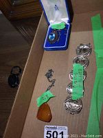 Photo of necklace with amber colored triangular pendant, necklace with blue decorative pendant in a display box, and Egyptian silver bracelet with engravings