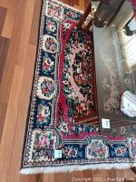 Full view of rectangular handwoven area rug placed on wooden floor with visible floral and geometric patterns in red, blue, cream and pink.