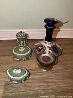 Photo showing three Wedgwood green jasperware dishes, glass candle holder, and decorative wine decanter against wall and wooden floor.