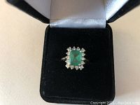 Ring in black velvet box showing emerald center and diamond halo