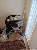 Evolution Folding Walker with seat and storage pouch against wall near door, with keys and papers on seat.