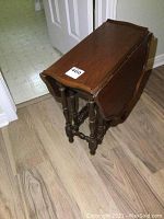 Angle view of folded gateleg side table showing dark wood finish, turned legs, and curved top edges.