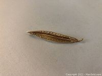 Close up of elongated leaf shaped gold brooch with textured surface and smooth back