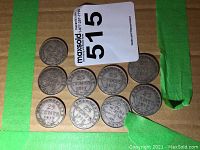 Nine coins arranged on cardboard, reverse side visible under green tape
