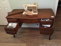 Full front view of the sewing table with open drawers showing sewing notions and vintage Singer sewing machine on top with manual.