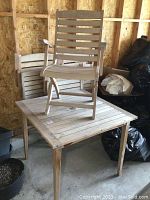 Overall view of wood patio table with one folding armchair placed on top in indoor setting