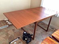 Full view of the extended teak table showing overall form, center seam, and leg style