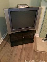 Full front view of Sony Trinitron 28-inch CRT TV on black laminated stand with glass doors.