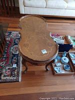 Full view of vintage wooden coffee table with floral marquetry top and carved legs on a hardwood floor near a patterned rug.