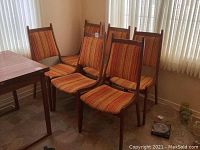 Six wood-framed dining chairs with striped orange and yellow upholstery arranged near a table