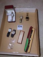 Overview photo of six vintage watches with metal and leather bands, watch parts included, placed in cardboard box.