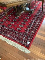 Full view of red wool area rug under dining table, shows repeating medallion design and ivory fringe