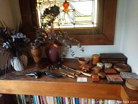 Overview of dried flower arrangements, cutlery, and various boxes on a wooden table with stained glass window behind