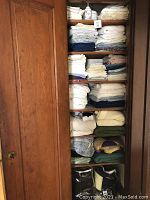 Wide view of wooden closet shelf filled with folded linens including towels, sheets, and blankets