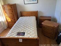 Full view of the wooden twin bed showing the sleigh-style headboard and footboard, mattress on top, tall dresser in corner, and two nightstands beside the bed.