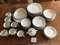Full display of the china set on a wooden table, showing multiple plates, bowls, cups, saucers and a sugar bowl.