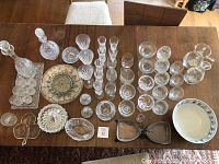 Overview photo of multiple crystal and glass items on wooden table, including glasses, decanters, plates, ashtrays, handpainted pitcher and vase.