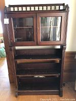 Front view of vintage wooden display case showing glass doors upper section, spindle top detail, and three open shelves below.
