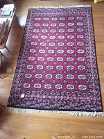 Full view of the large rectangular floor rug laid on hardwood floor, showing repeating oval floral medallion pattern with bordered edges and fringe ends.