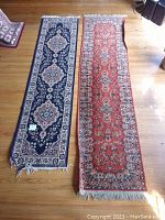 Full view of two floor runner rugs laid side by side on wooden floor showing design, color, and fringe.