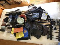 Top-down view of assorted handbags, purses, wallets, eyeglasses with cases, and a metal luggage cart laid out on a white surface.