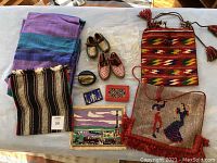 Photo showing the full lot including two woven textile sheets, two pairs of small mukluk-style shoes, multiple colorful woven bags, beaded coin purse, leather wallet, and decorative fabric pieces.