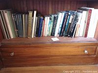 Books on wooden shelf showing entire lot of mythology, history, and anthropology books, arranged in a row with varied spine colors and titles.