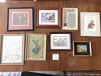 Seven framed pieces including handpainted floral art, lithographs, music sheets, and prints arranged on tabletop