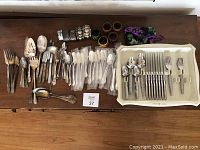 Wide view of assorted flatware and napkin rings spread on a table showing quantity and variety.