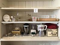 Shelf with various small kitchen and food preparation items including bowls, measuring cup, rolling pin, blender base, pasta machine, stovetop espresso pot, and other small containers.
