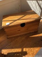 Wooden chest placed on wooden floor in bright natural light, showing rectangular shape and wood grain.