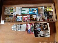 Light bulbs and batteries arranged on a wood shelf with work gloves and some household utility items
