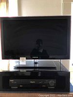 Samsung 31 inch TV on top of black lacquer stand with Toshiba VHS player underneath.