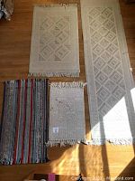 Four rugs arranged on wood floor: off white runner, off white medium rug, small off white rug with stains, blue striped rug