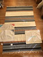 Photo showing three rugs laid flat on wooden floor with visible stripes and fringe, worn and discolored areas noted
