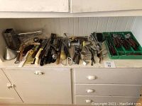 Wide view of vintage cutlery and kitchen tools laid out on a white cabinet with green flatware trays, showing diverse kitchen utensils in various conditions.