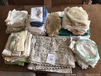 Overview of multiple piles of vintage doilies, napkins, and linens in various colors and sizes arranged on a table.