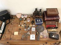 Top-down view of a wooden desk with a collection of jewelry including necklaces, pins, brooches, small boxes, and personal effects spread out neatly.