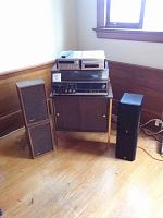 Wide angle photo showing complete stereo system setup including Sony console system on top of a wood-finish record cabinet, Yamaha stereo receiver and CD player on top, and a pair of speakers on either side.