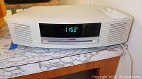 Front view of white Bose Wave music system showing digital clock 11:52 and CD slot with Bose logo above it.