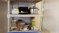 Two shelves holding various kitchen and household items including a Farberware pot, hand mixer, and accessories.