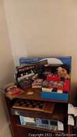 Photo showing various game sets placed on wooden shelves, including poker sets, electronic game, checker board and card decks.