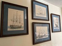 Four framed nautical ship prints hanging on wall, blue mats and dark carved wood frames