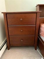 Front view of a wooden nightstand with three drawers, medium brown finish and round wooden knobs. Shows some scratches and signs of wear.